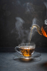A man pouring aromatic hot tea into glass cup on black table, closeup