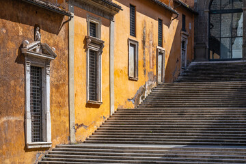 Visitors ascend the grand staircase at Capitoline Square in Rome, Italy, surrounded by vivid orange walls and architectural details typical of the historic district.