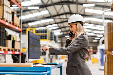 Female engineer, project manager standing in modern industrial factory by computer, making phone...