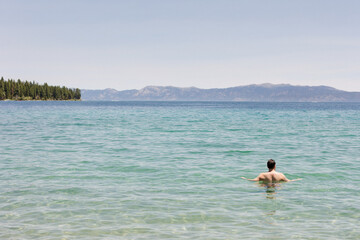 Person swimming in a clear, turquoise lake with distant mountains