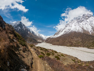 A panoramic view of a snow-capped mountain range. The sky is a clear blue, with a few puffy white...