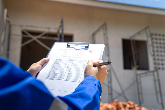 An architect is checking on house building quality checklist form to inspecting the progress with building house as blurred background. Construction industrial working scene, close-up.