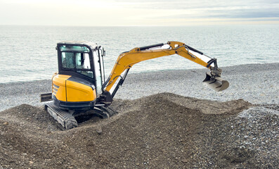 An excavator digs stone pebbles on the seashore