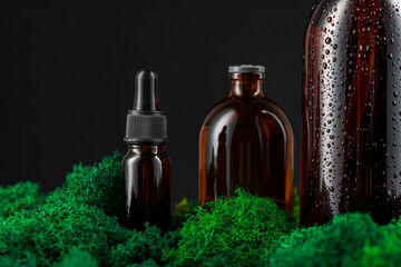 Dark glass bottles arranged on green moss against a black background