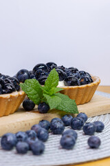 Close-up Blueberry tartlets on a small cutting board. blueberries around and mascarpone on the back