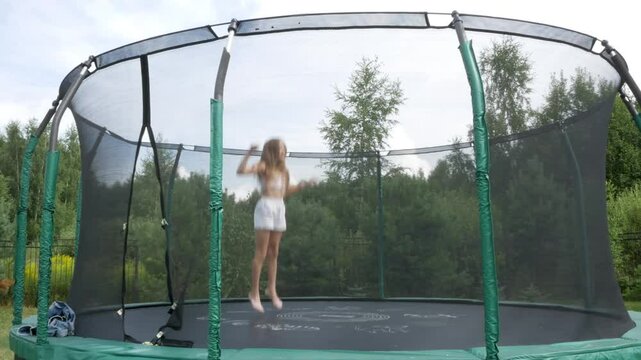 Happy teen girl jumping on a trampoline and doing a somersault in a jump in a backyard. Embracing Summer Fun. Entertainment for children