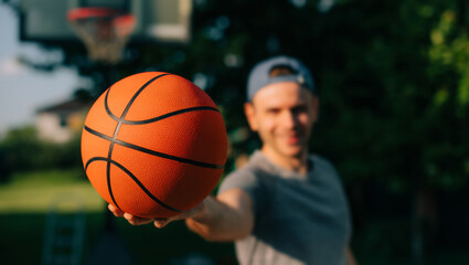 A man in a backward cap extends a basketball towards the camera, with the vibrant orange ball in...