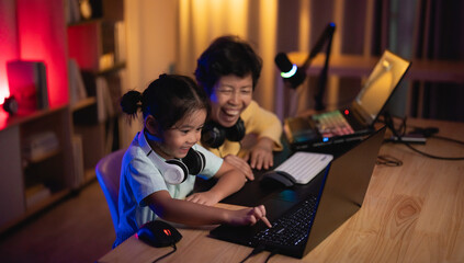 Asian woman and a child are playing a video game on a laptop. The woman is smiling and the child is pointing at the screen