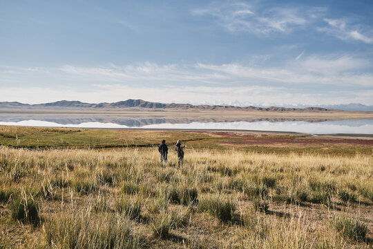 Two people walking in a field beside a reflective lake
