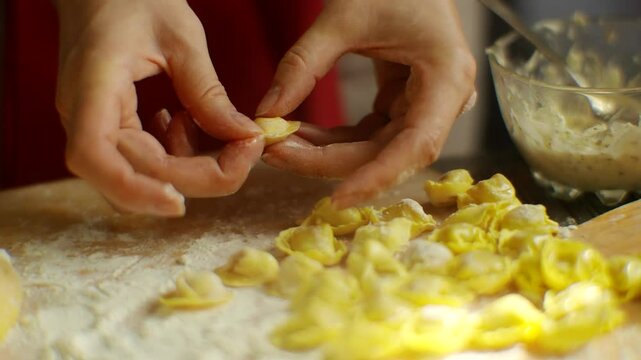 Close-up of hands preparing homemade tortellini pasta on wooden surface 