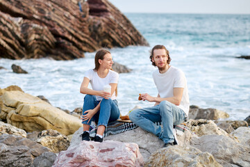 Fototapeta premium Man and Woman Sitting on Rocks by the Ocean