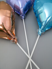 Three foil heart-shaped balloons on a stick on a gray background