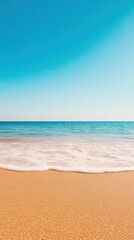 Obraz premium A serene beach view featuring soft sand and gentle waves under a clear blue sky, perfect for relaxation and vacation imagery.