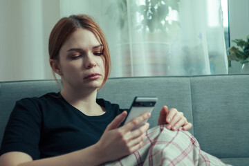 The girl is procrastinating: lying with a phone in her hands, a lazy expression on her face, a concentrated look