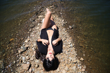 Pretty young brunette latin woman with red lips and dressed in black shirt and black bikini lying...