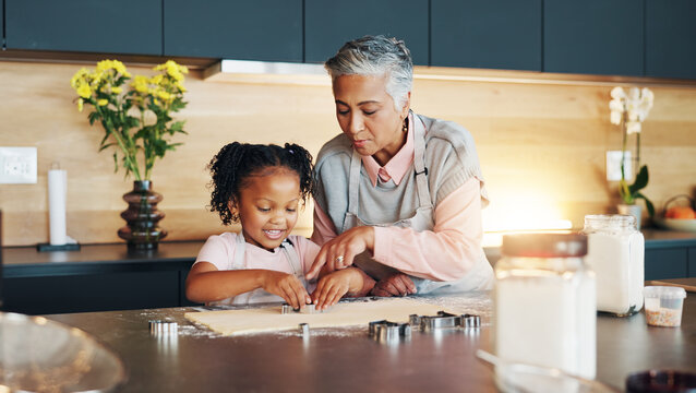 Grandma, little girl and baking with cookie cutter on table in kitchen for learning, teaching or making dough at home. Grandmother, child or junior baker with shapes for dessert or recipe at house