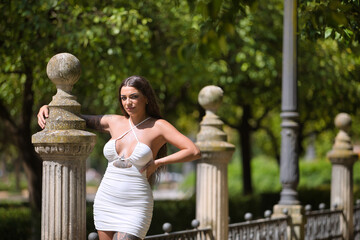 A young, dark-haired, beautiful woman, heavily tattooed, in a white dress, clinging to a stone...