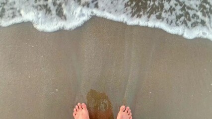 Feet in the Sand. A pair of feet standing on a sandy beach with waves lapping at the toes.
