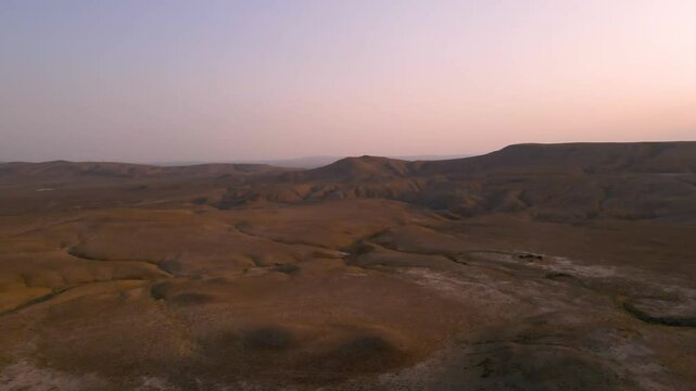 Drone shot flying over the desert landscapes in the Qobustan National Park in Azerbaijan at sunset on a clear day.