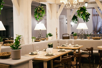 Christmas light modern interior of the restaurant with greenery with pleasant cozy lighting and festive table setting with glasses.
