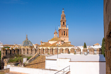 The image presents a church tower rising above walls with a blue dome in view, embodying historic religious architecture, cultural heritage, and the tranquility of a clear blue sky in Carmona Spain