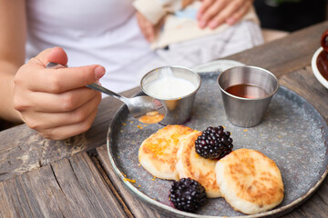 Unrecognizable female eating gourmet blueberry pancakes with newborn child in hands enjoying fresh morning healthy snack dessert with fresh ingredients for diet-friendly meal at table in outdoor cafe