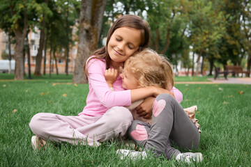 Fototapeta premium Charming little sisters enjoying time together in nature with satisfied expressions and joyful faces hugging each other spending summer time together in park