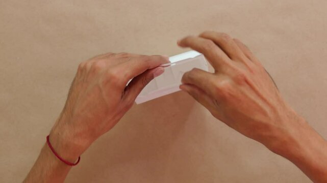 Hands assembling white confectionery box on beige surface, close-up