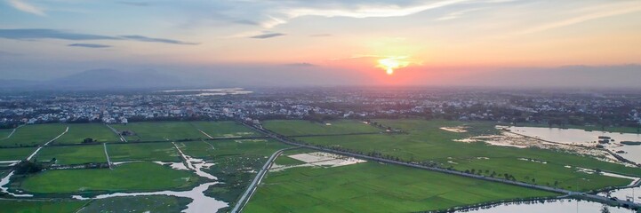 Fototapeta premium Aerial view of lush green rice fields and a peaceful town at sunrise, perfect for Asian rural landscapes and nature concepts