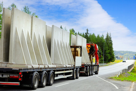 Volvo FH truck and Naerko trailer transporting tall precast concrete components in highway traffic, rear view. 