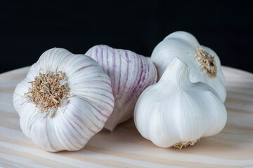 Fresh purple garlic heads and cloves on a rustic wooden plate with black background.