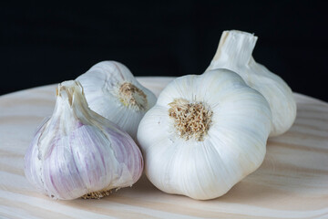 Fresh purple garlic heads and cloves on a rustic wooden plate with black background.