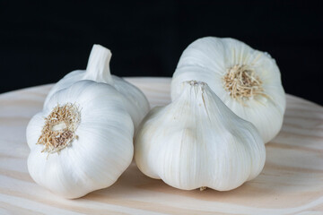 Fresh white garlic heads and cloves on a rustic wooden plate with black background.