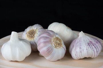 Fresh pink garlic heads and cloves on a rustic wooden plate with black background.