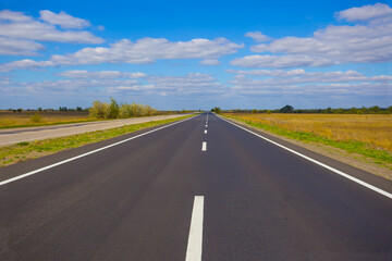 long asphalt road among green plain under a blue cloudy sky
