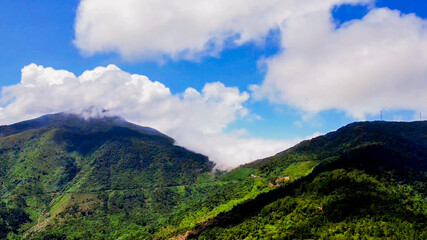 Fototapeta premium Lush green mountain range beneath a blue sky and fluffy clouds, capturing the beauty of nature and scenic landscapes
