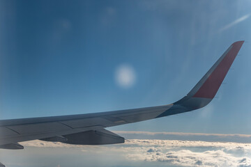 Wing of an airplane flying above the clouds in the blue sky.