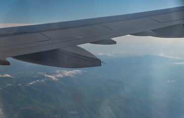 Obraz premium Wing of an airplane flying above the clouds in the blue sky.
