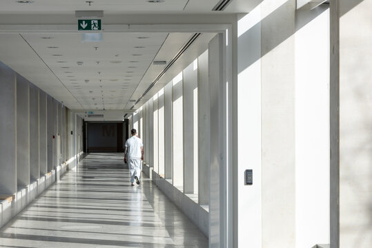 A medical worker walks along a long white corridor in a hospital