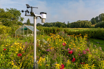 Private Wetterstation in einem Garten mit Gewächsahus und blühenden Sommerblumen