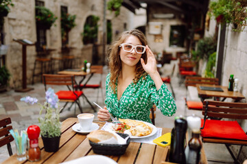 A young woman enjoys breakfast in a charming café courtyard adorned with plants on a sunny morning. Parmesan cheese. Travel, tourism, food and drink.