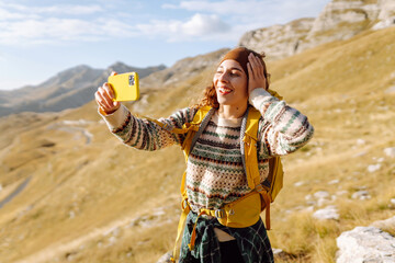 A young woman with a backpack is happily taking a selfie in the mountains. Nature freedom adventure, happy vacation. Blogging.