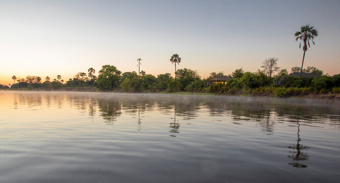 View of serene Zambezi river at sunset with lush vegetation and calm water, Victoria Falls, Zimbabwe.