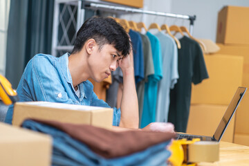 Fototapeta premium Young Asian man, distributor, online shop owner, small business owner, stands in warehouse, looking stressed and depressed when there are no orders.
