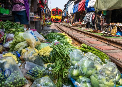 View of vibrant railway market with stalls selling fresh produce and a train passing through, Mae Klong, Thailand.