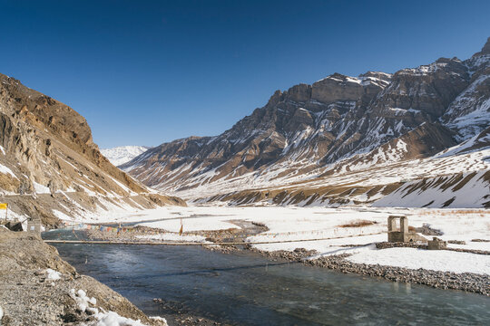 View of snow mountains and a river with rocks and a village in the remote Pin Parvati Valley, Kaza, Spiti Valley, India.