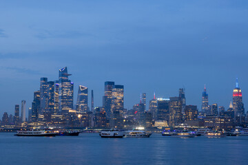View of vibrant cityscape with illuminated skyscrapers and Hudson River at blue hour, New York City, United States.
