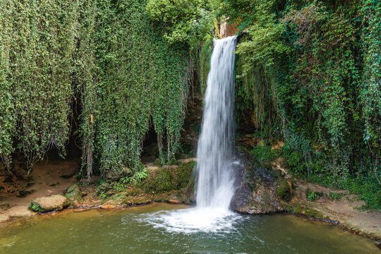 A serene waterfall cascades over rocks into a tranquil pool surrounded by lush greenery in a peaceful outdoor setting