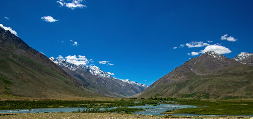 View of breathtaking snow-capped peaks and a serene river in the lush valley, Ghizer, Pakistan.