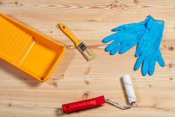 Paint tray, brush, roller and gloves on a wooden background.